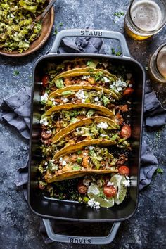 an image of mexican food in a baking dish on a table with beer and other foods