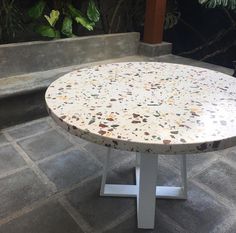 a white table sitting on top of a stone floor next to a plant filled area