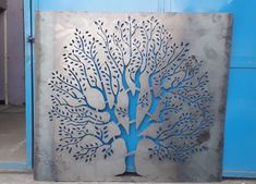 a large metal tree with blue leaves on it's sides is shown in front of a blue door