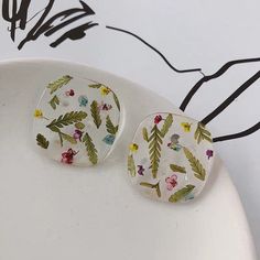 two glass cabochons with flowers and leaves on them sitting on a white plate