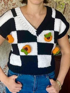 a woman wearing a black and white sweater with orange flowers on the front, standing in front of a floral wallpaper