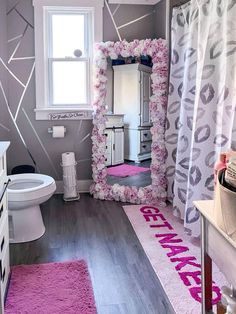 a bathroom decorated in pink and gray with flowers on the shower curtain, toilet seat cover, sink vanity and mirror