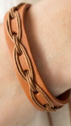 a close up of a person wearing a brown leather bracelet with braiding on it