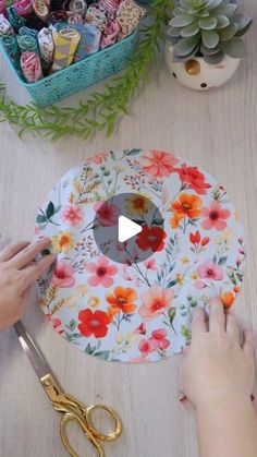 a person cutting up a flowered paper plate with scissors and glue on it, surrounded by other crafting supplies