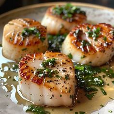 four sea scallops on a plate with parsley and seasoning sprinkles