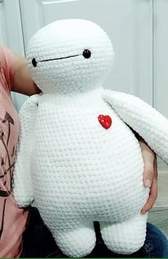 a person holding a white crocheted stuffed animal with a red heart on it's chest