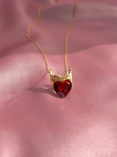 a red heart shaped pendant on a gold chain with angel wings hanging from it's center