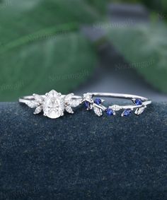 two wedding rings with blue and white stones on top of each other, next to a leafy plant