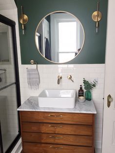 a white sink sitting under a round mirror on top of a wooden cabinet in a bathroom