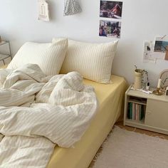 an unmade bed in a bedroom with white walls and pictures hanging on the wall