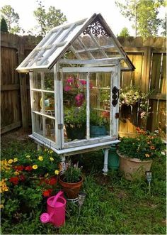 a small white greenhouse in the middle of some flowers and potted plants on the ground