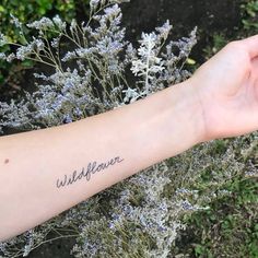 a woman's arm with the word wildflower written on it and flowers in the background