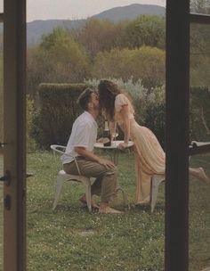 a man and woman sitting at a table in the middle of a field, kissing