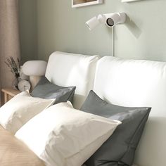 three pillows on a white couch in front of a wall mounted lamp and pictures above the headboard