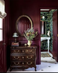 a room with red walls and a mirror on the wall next to a chest of drawers