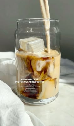 a glass filled with liquid and ice cubes sitting on top of a white table