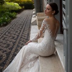 a woman in a wedding dress is sitting on the ledge looking off into the distance