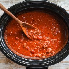 a wooden spoon in a slow cooker filled with chili sauce and meatballs, ready to be cooked