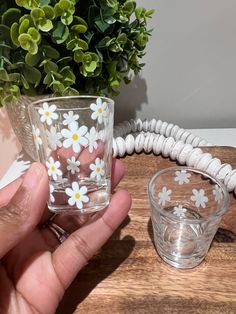 a hand holding a glass with white flowers on it and a phone in the background