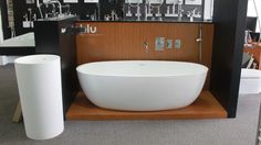 a large white bath tub sitting on top of a wooden shelf next to a toilet