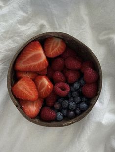 strawberries, blueberries and raspberries in a bowl on a white sheet