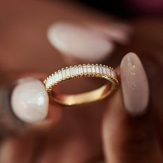 a close up of a person's hand holding a gold ring with white stones