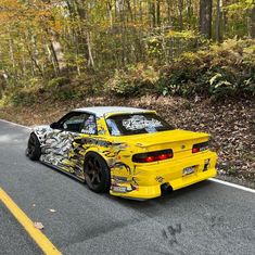 the yellow car is parked on the side of the road in front of some trees