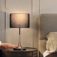 a person's hand next to a nightstand with a lamp on it