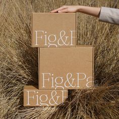 two cardboard boxes sitting in the middle of some dry grass with handwritten words on them