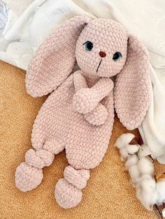 a pink knitted bunny laying on top of a bed next to a pile of cotton