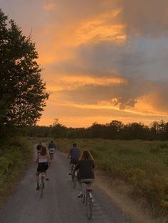 three people riding bikes down a dirt road at sunset or dawn with clouds in the sky