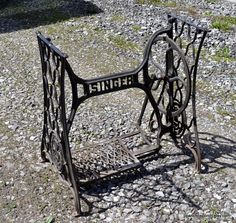 an old iron sewing machine sitting on the ground next to some rocks and grass in front of a building