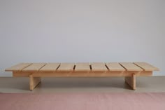 a wooden bench sitting on top of a pink rug in front of a white wall