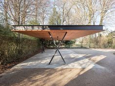 a large wooden table sitting on top of a cement floor in front of some trees