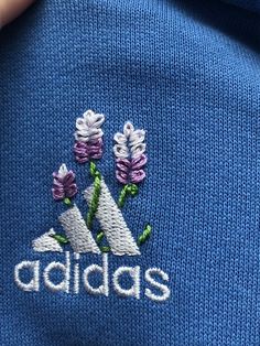 the adidas logo is embroidered on a blue sweater with purple and white flowers in it