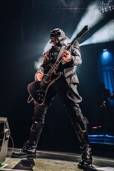 a man with a guitar in his hand and wearing all black on stage at a concert