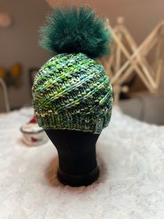 a knitted hat with a green pom - pom sitting on top of a head