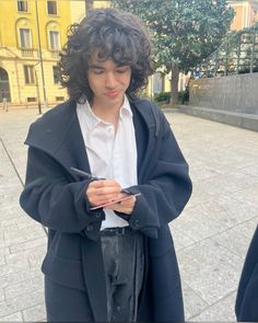 a young man standing in front of a building looking at his cell phone while wearing a coat