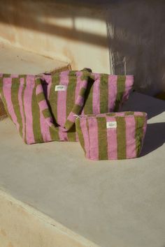 three pink and green striped bags sitting on top of a cement floor next to a wall