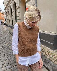 a woman is walking down the street wearing a brown sweater vest