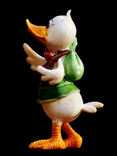 a figurine of a duck wearing a green shirt and orange boots, holding a piece of wood