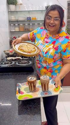 a woman is holding a tray with two cups of coffee and a pizza on it