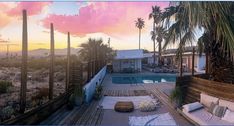 the sun is setting over an outdoor pool and deck area with palm trees in the foreground