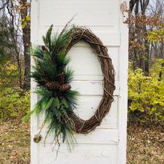 a wreath is hanging on the side of a white door with pine cones and greenery