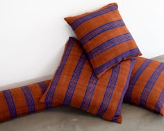 three orange and blue striped pillows stacked on top of each other in front of a white wall