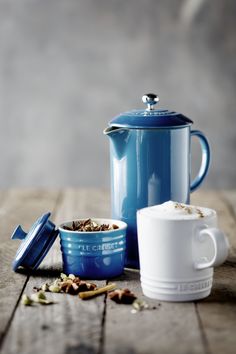 a blue coffee pot sitting on top of a wooden table next to a cup and saucer