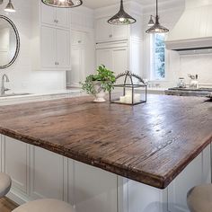 a large wooden counter top in a kitchen next to stools and an island with lights