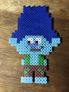 a pixel art piece made out of legos on a wooden table with a blue hat and green shirt