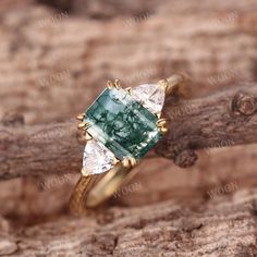 a green and white diamond ring sitting on top of a tree branch in front of a log