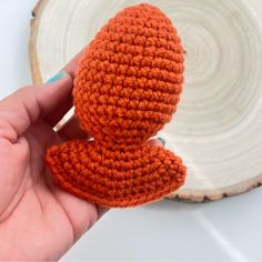 an orange crocheted stuffed animal sitting on top of a wooden slice in someone's hand